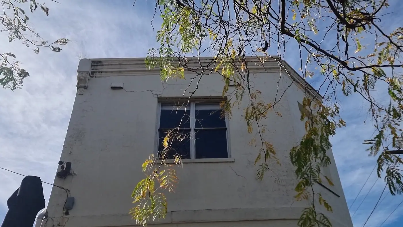 Mitte's white-rendered two-storey corner building under gum-tree branches and a blue sky