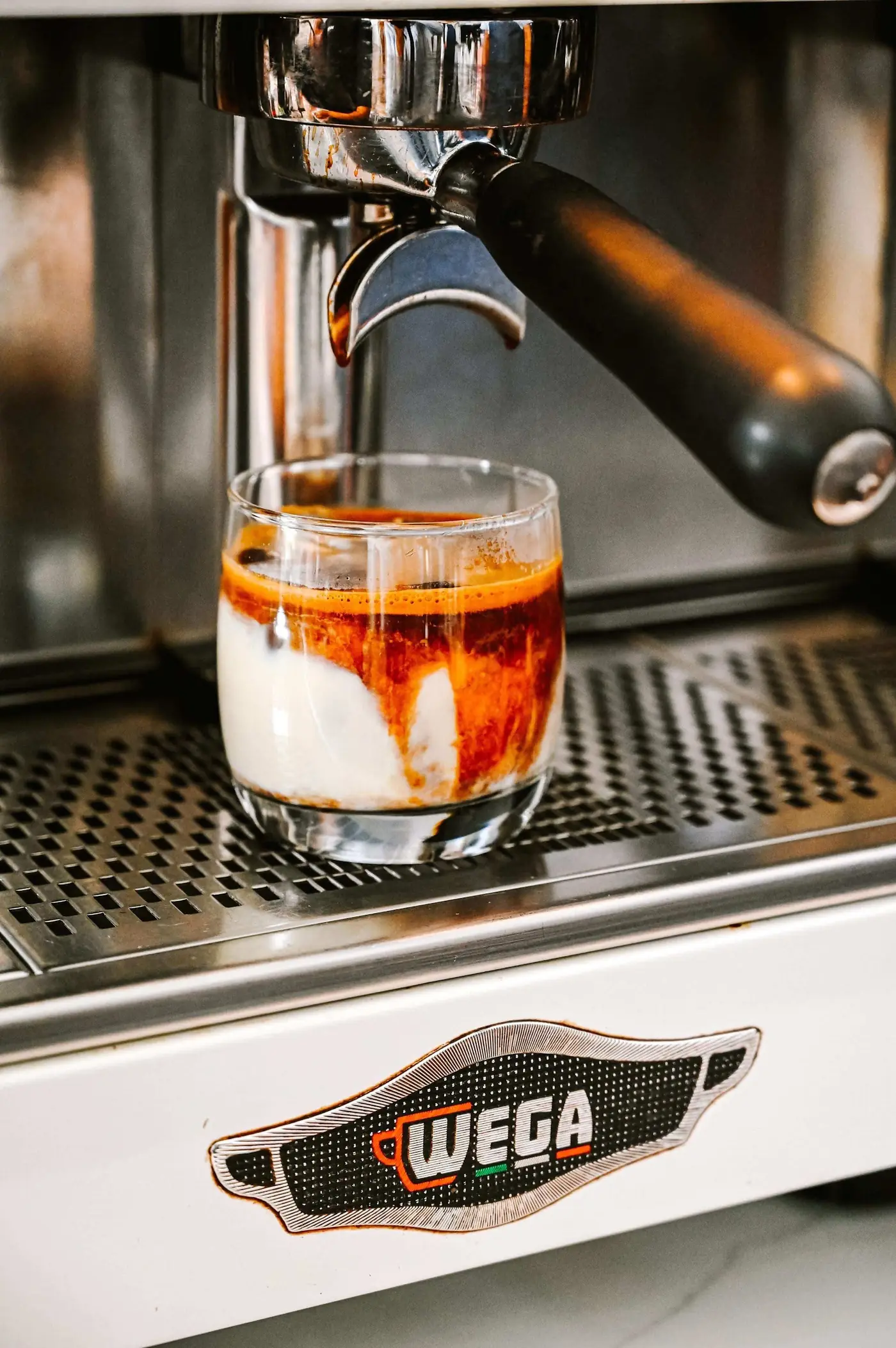 Espresso pouring over cold milk in a short glass on Mitte's white WEGA machine