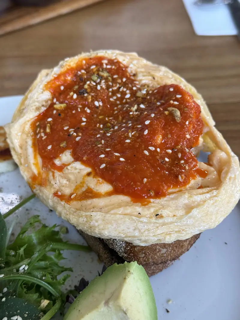 Harissa scrambled eggs with sesame on toast, avocado and greens