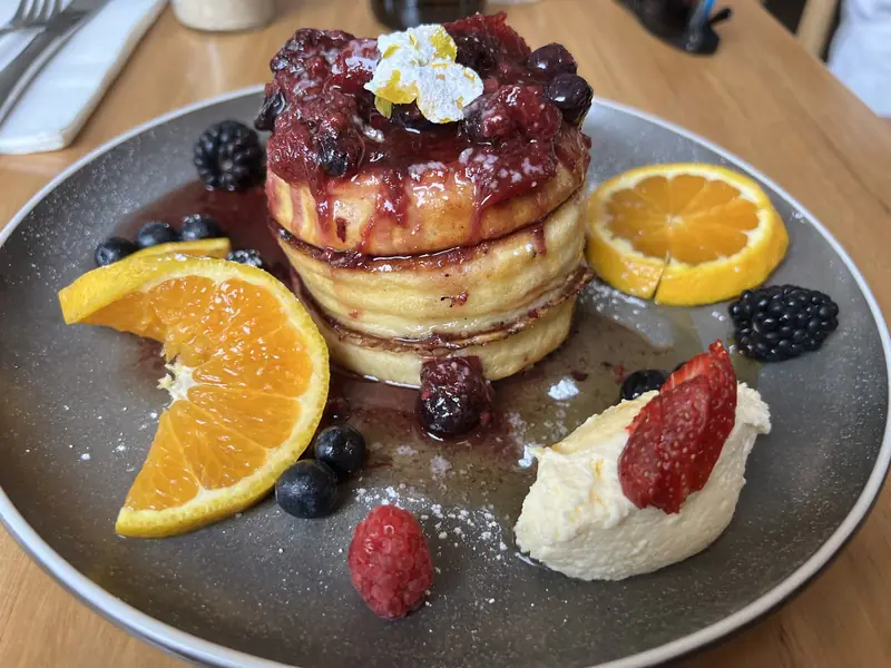 Stacked pancakes with berry compote, orange slices, fresh berries and cream