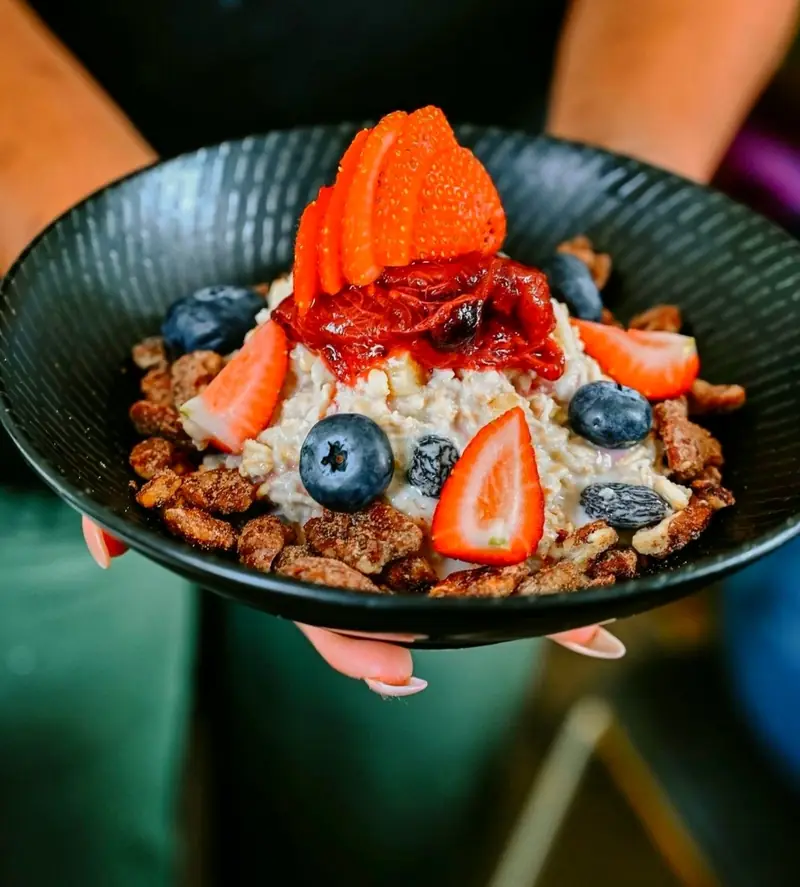 Porridge in a dark bowl with strawberries, blueberries and candied nuts